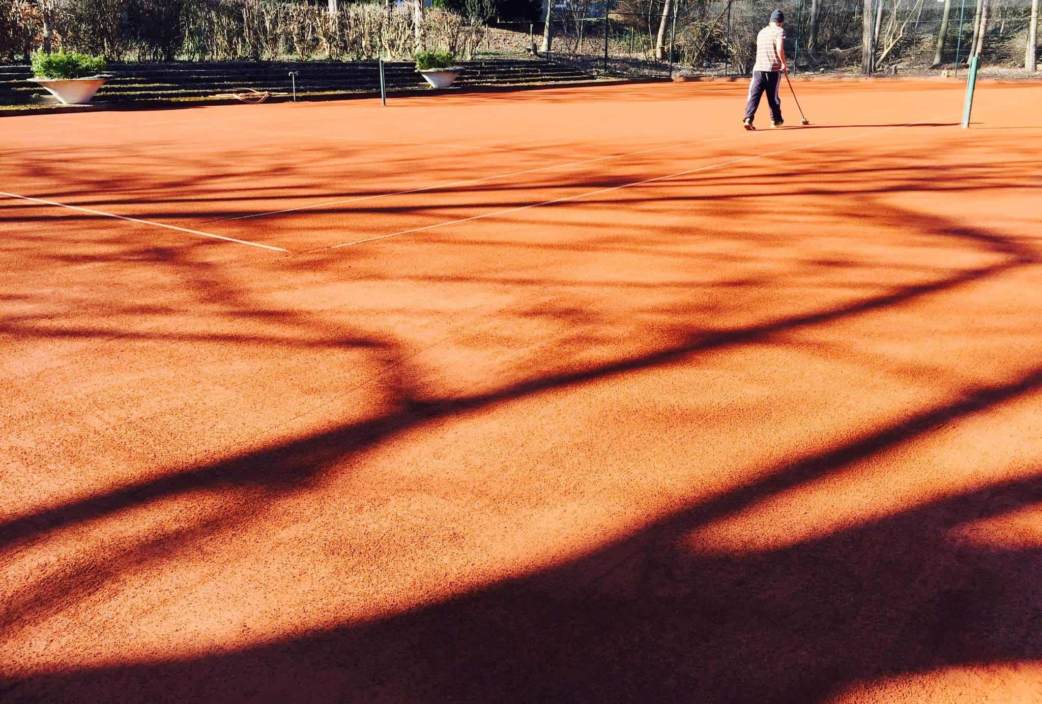 Sandplatz im Licht der Bäume, im Hintergrund wird der Platz abgezogen